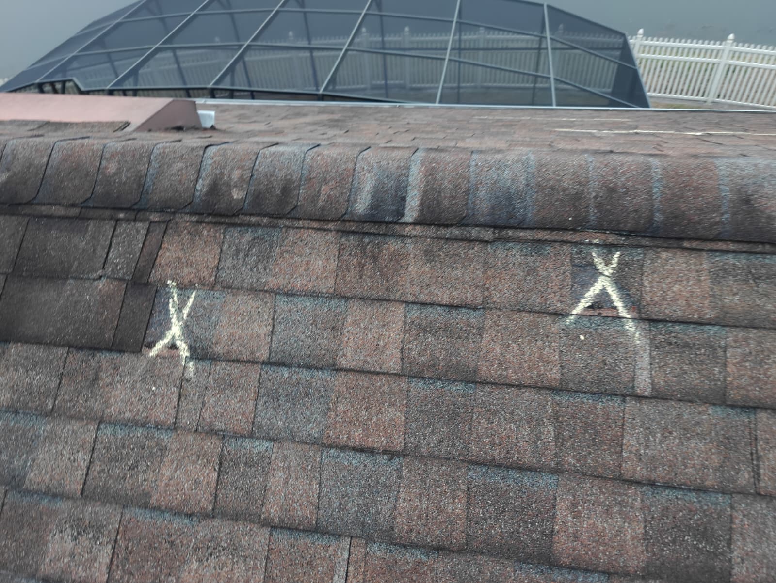 Chalk-marked damaged shingles along a roof slope during an insurance inspection